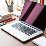 Notebook sobre mesa com livros e materiais de estudo.