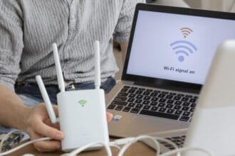 Pessoa preocupada segurando roteador ao lado de notebook em casa.