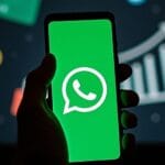 Celular com logo do WhatsApp e mão suspeita ao fundo
