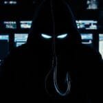 Hacker encapuzado em frente a telas de computador brilhantes