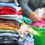 Roupas coloridas ao lado de lixeira de reciclagem verde
