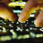Mãos digitando rapidamente em um teclado iluminado por tela de computador.